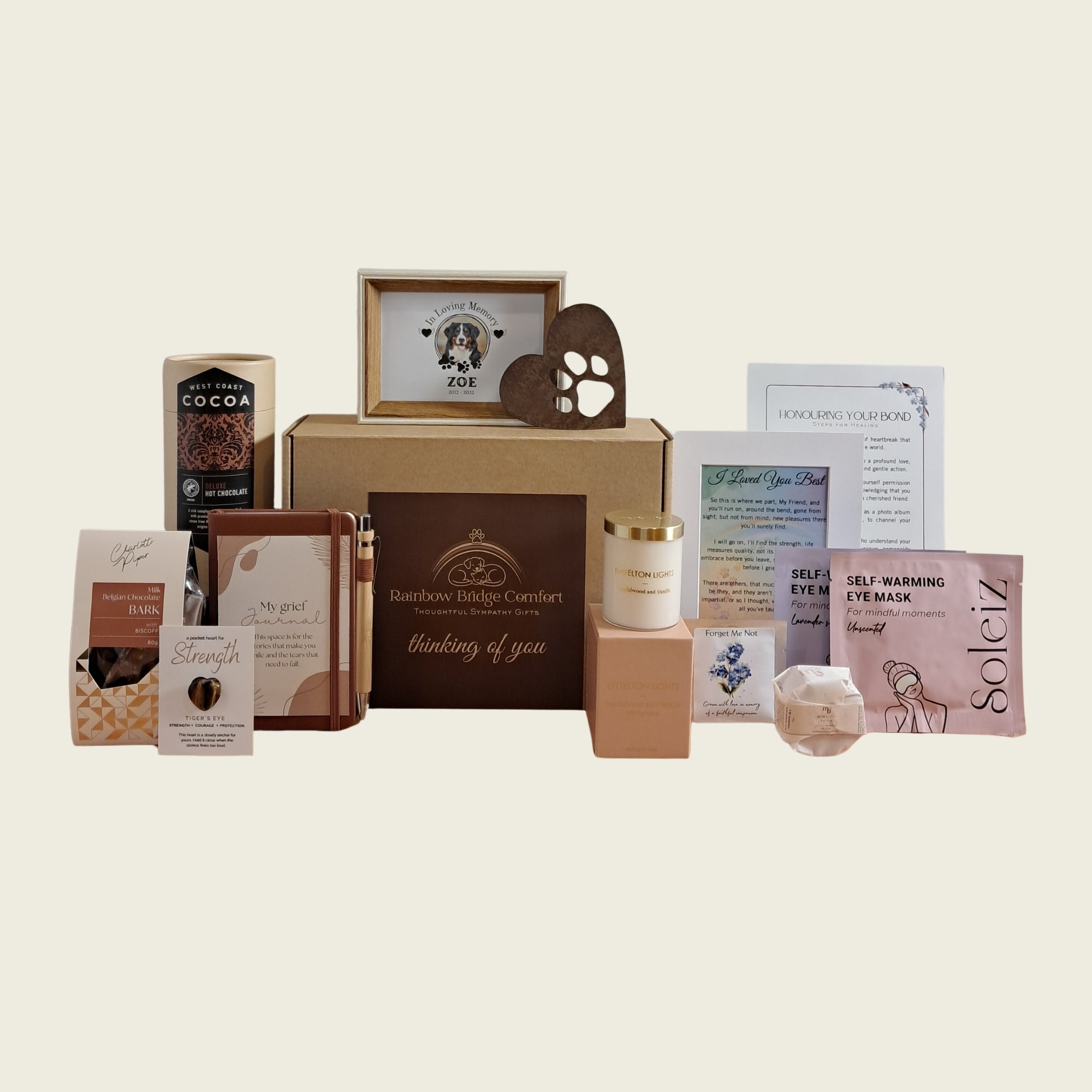 Complete Comfort pet sympathy gift box by Rainbow Bridge Comfort, featuring a curated collection of grief support items. Includes personalised dog memorial photo frame, metal heart paw ornament, journal with pen, luxury candle, self-warming eye masks, West Coast Cocoa, gourmet chocolate bark, Forget-Me-Not seeds, and a tiger's eye pocket stone.