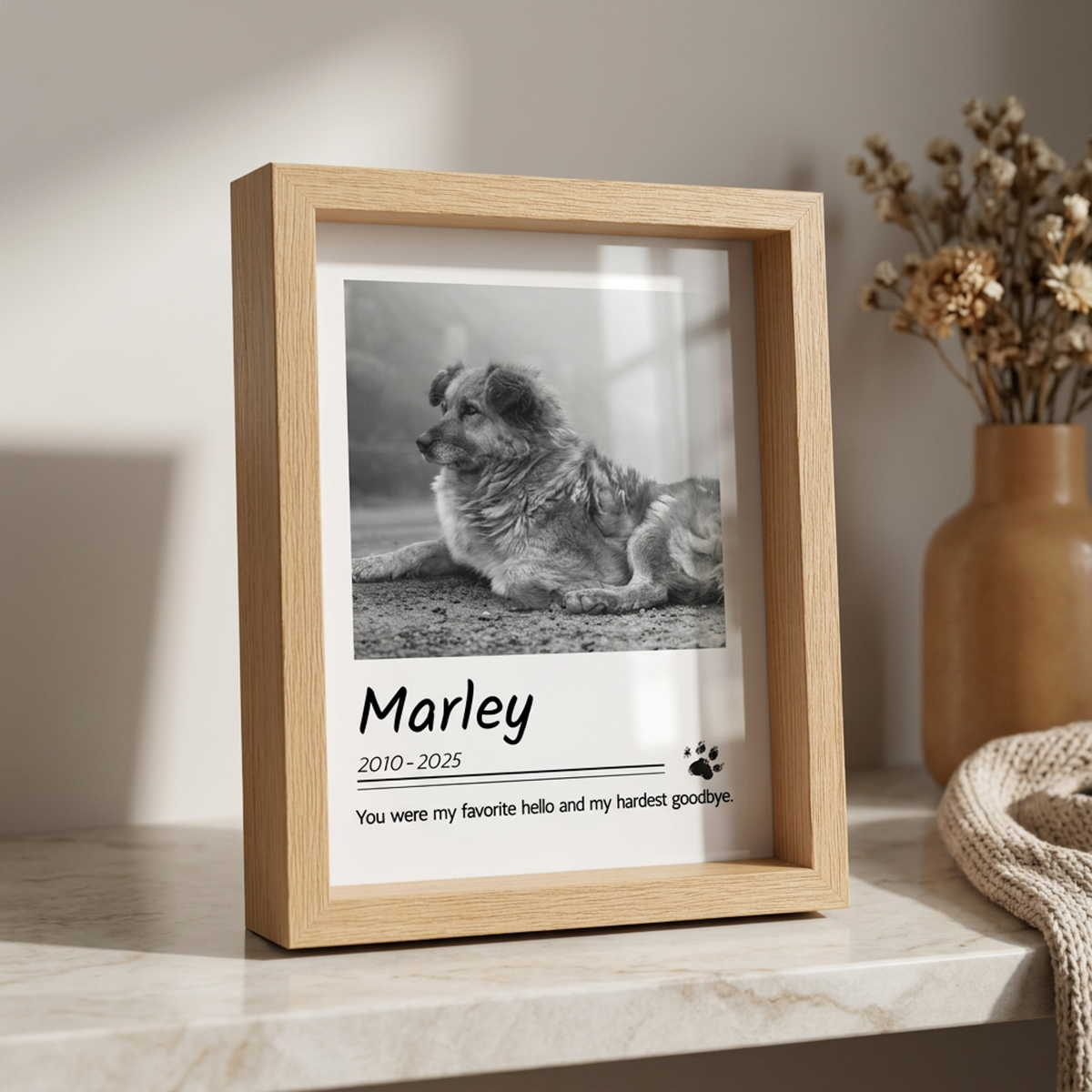 A light natural wood shadow box frame displayed on a marble surface, containing a black and white photo of a dog and a personalized memorial text for 'Marley'.