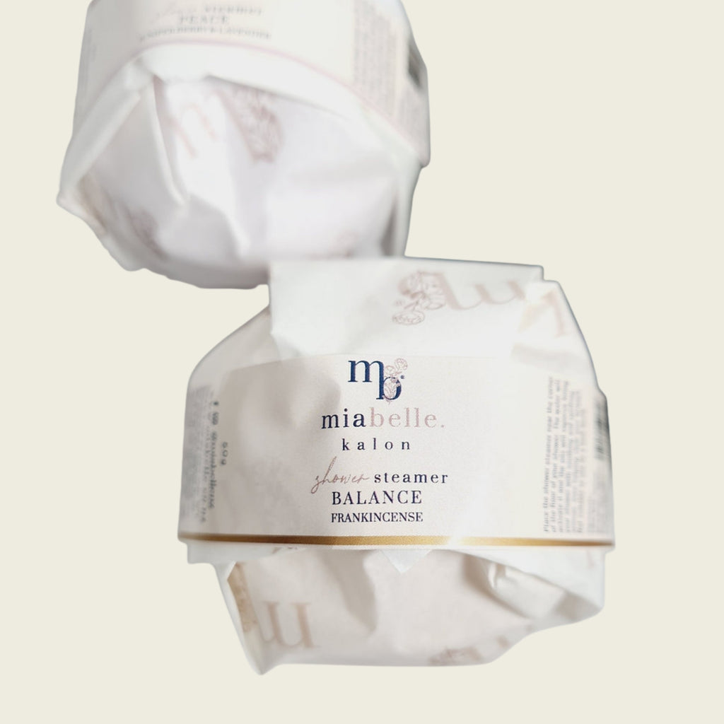 Two Mia Belle aromatherapy shower steamers in white and gold packaging, included in the Remembrance Deluxe pet sympathy gift box.