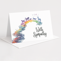 A white greeting card standing upright on a white envelope against a light gray background. The card features a colorful watercolor rainbow with silhouettes of cats and birds along the top and the words 'With Sympathy' in black script on the right.