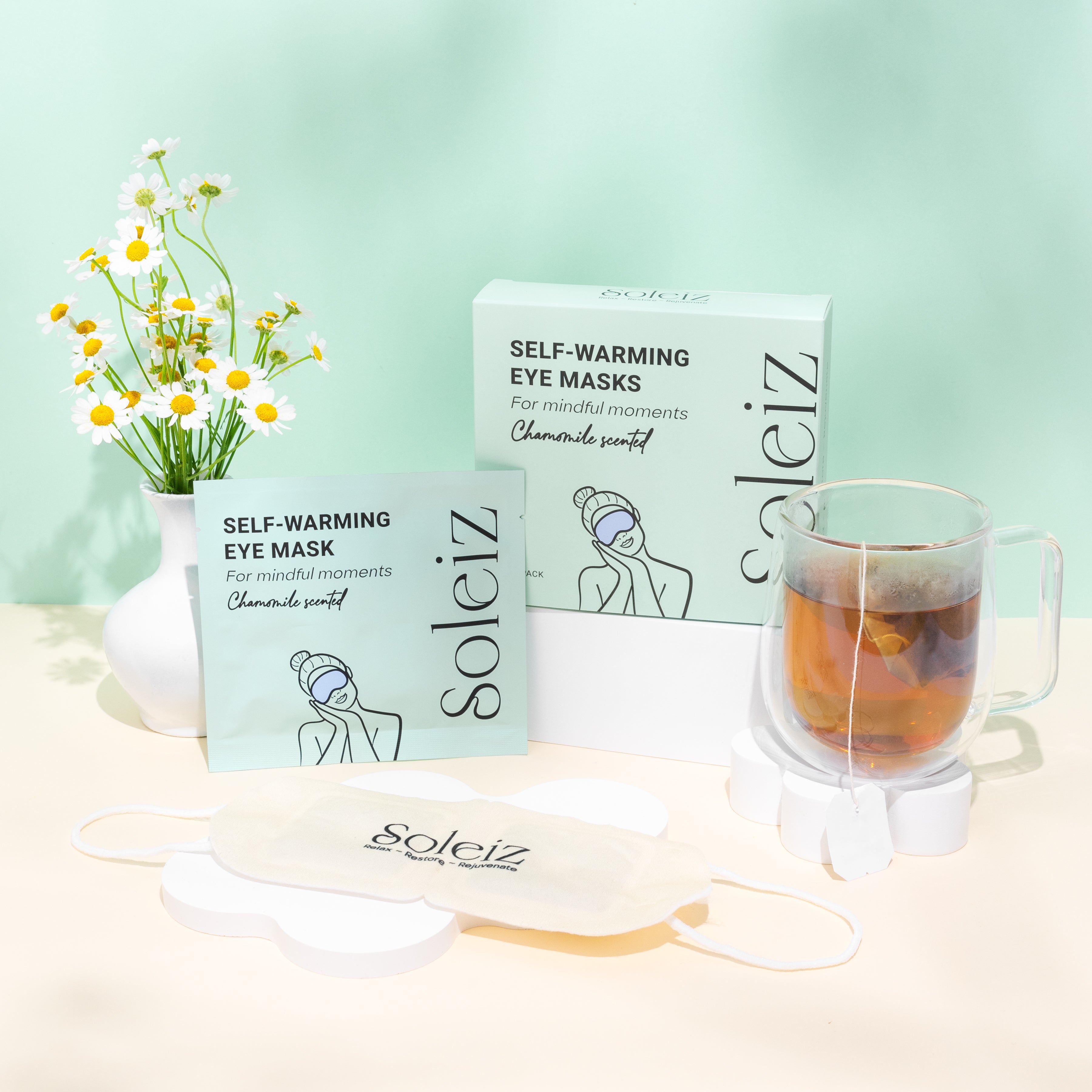 Soleiz self-warming eye masks with a cup of tea and flowers on a light green background